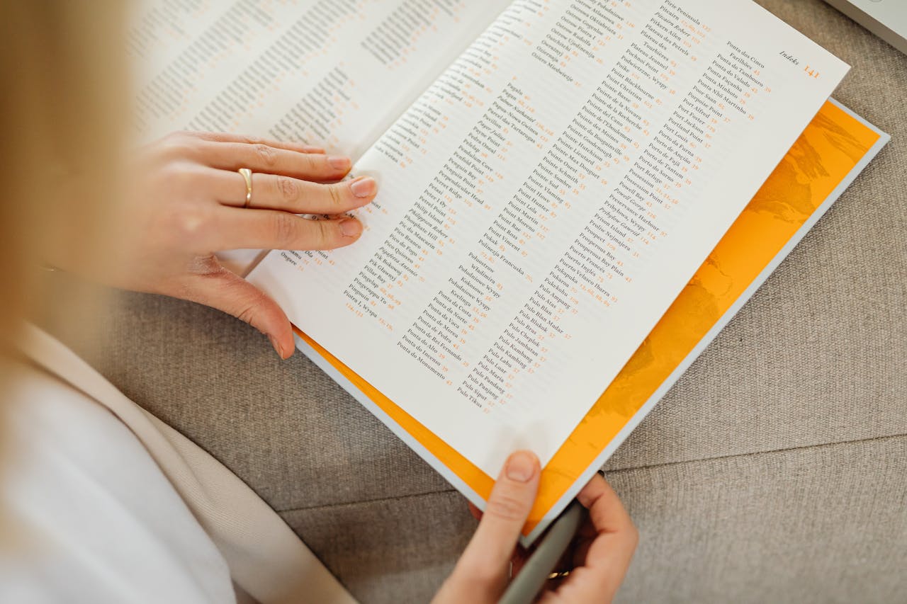 Close-up of a womans hands holding an open book on a sofa, focusing on text details.